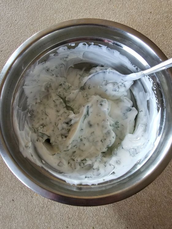 Greek yogurt, minced mint, and minced parsley mixed together in a metal bowl.