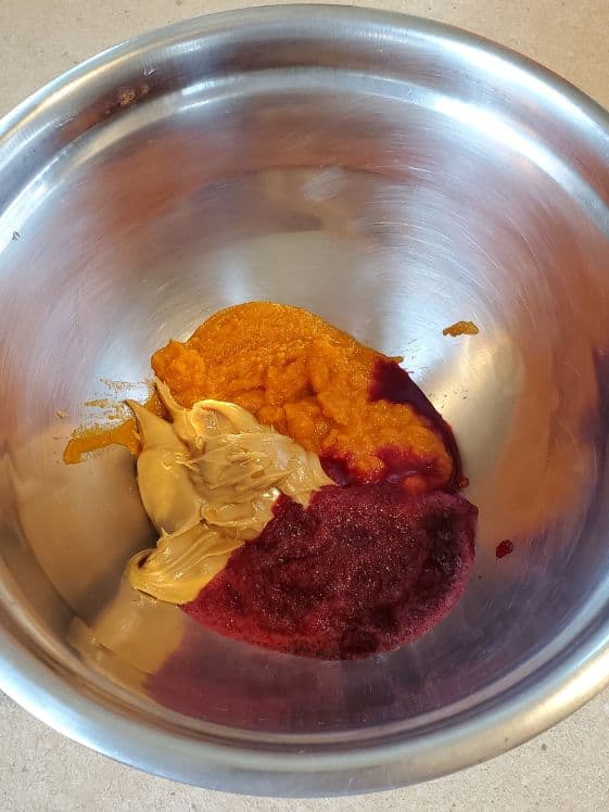 Peanut butter, pumpkin puree, and beet puree in a metal bowl.
