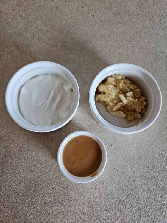 Greek yogurt, mashed banana, and peanut butter in three separate white bowls.
