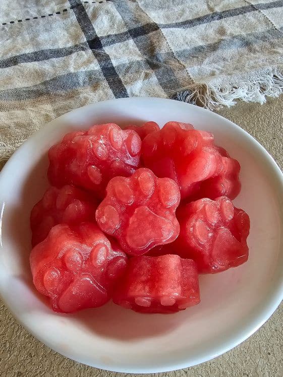 Paw shaped watermelon dog treats in a white bowl next to a towel on the counter.
