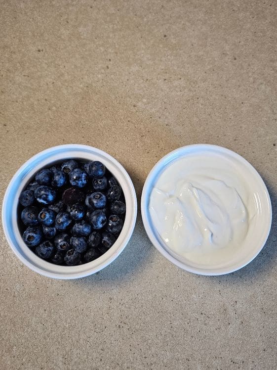 Blueberries and Greek yogurt in white bowls on a counter.