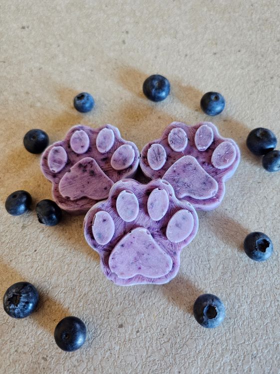 Three paw shaped frozen blueberry treats on a counter with blueberries around them.