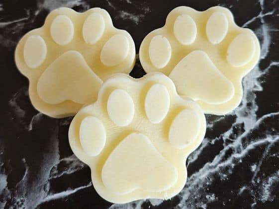 3 paw shaped frozen pineapple dog treats on a marble background