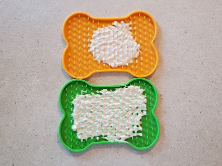 2 bone shaped lick mats with filling spread on them.