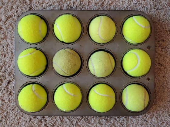 A dozen tennis balls covering all the cups in a muffin tin.