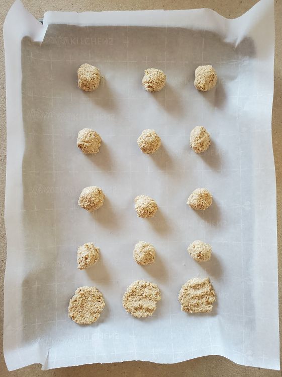 Oatmeal applesauce treat balls on a cookie sheet. 3 have been flattened for baking.