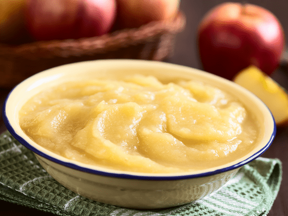 A bowl of applesauce with apples in the background.