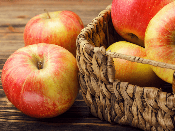 Two apples next to a basket of apples.