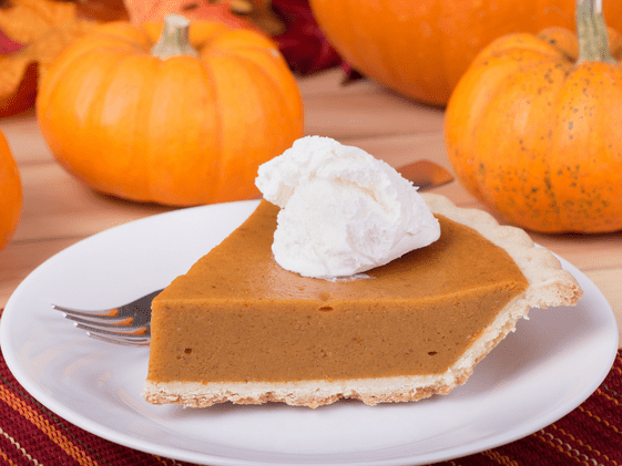 A slice of pumpkin pie with whipped topping on it. Small pumpkins are in the background.