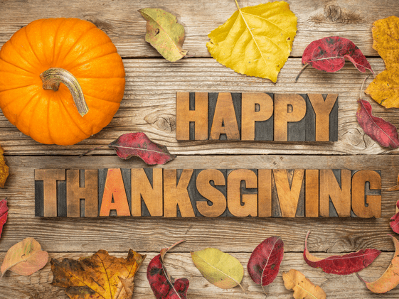 A pumpkin and fall leaves on a wood background with the words Happy Thanksgiving.
