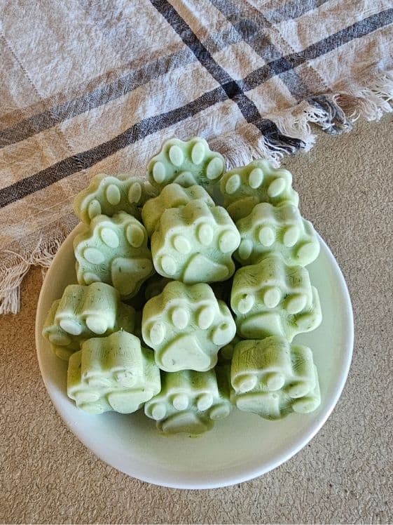 A bowl of paw shaped frozen fresh breath dog treats in a white bowl next to a linen towel.