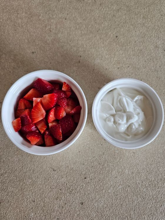 A bowl of chopped strawberries and a second bowl of yogurt.