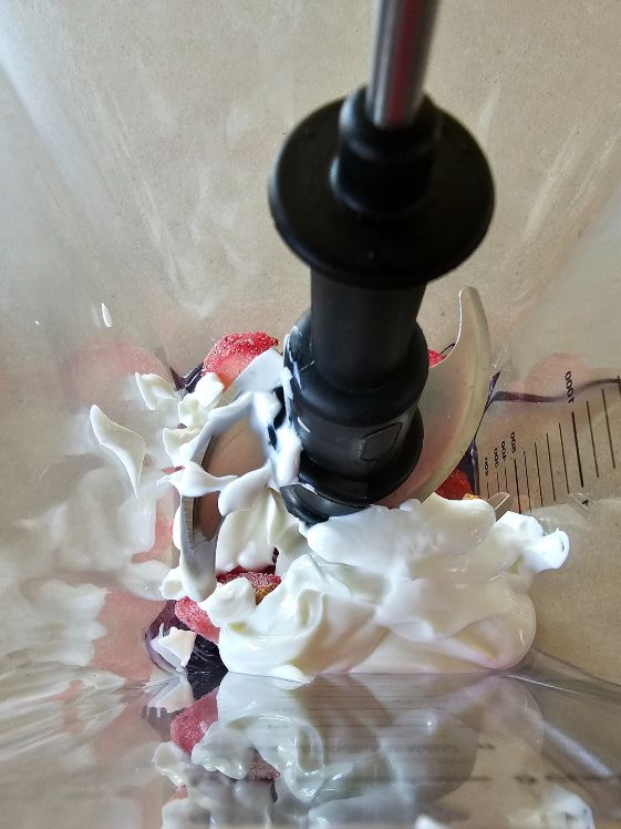 Frozen strawberries underneath Greek yogurt in a blender.
