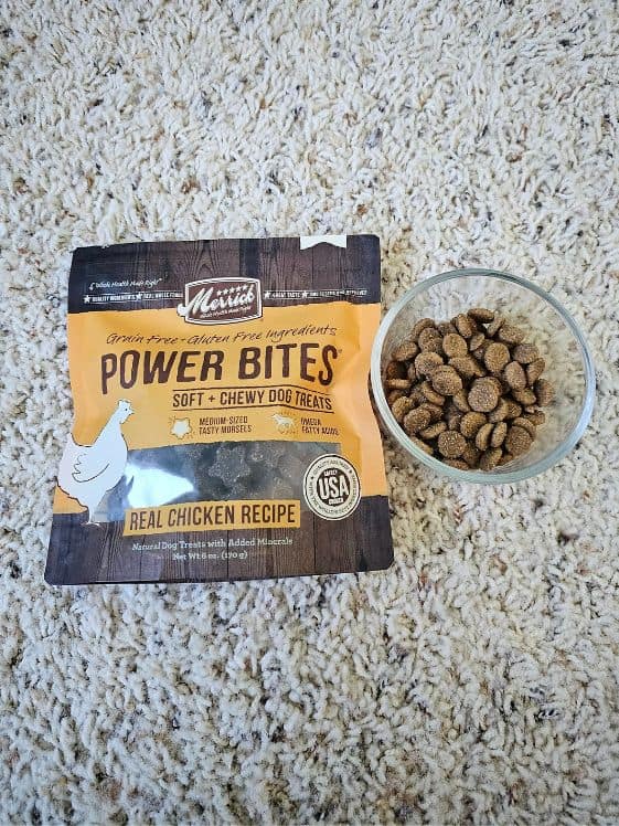 A bag of dog treats next to a glass bowl of dog kibble.