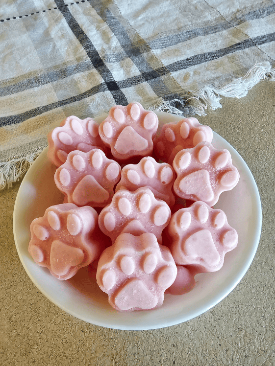 Paw shaped watermelon and Greek yogurt dog treats in a white bowl in front of a towel.