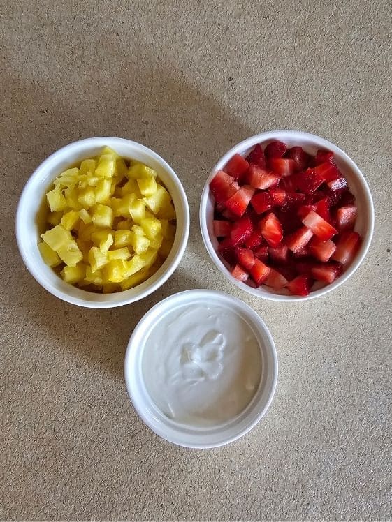 Pineapple chunks, diced strawberries, and Greek yogurt in individual white bowls.