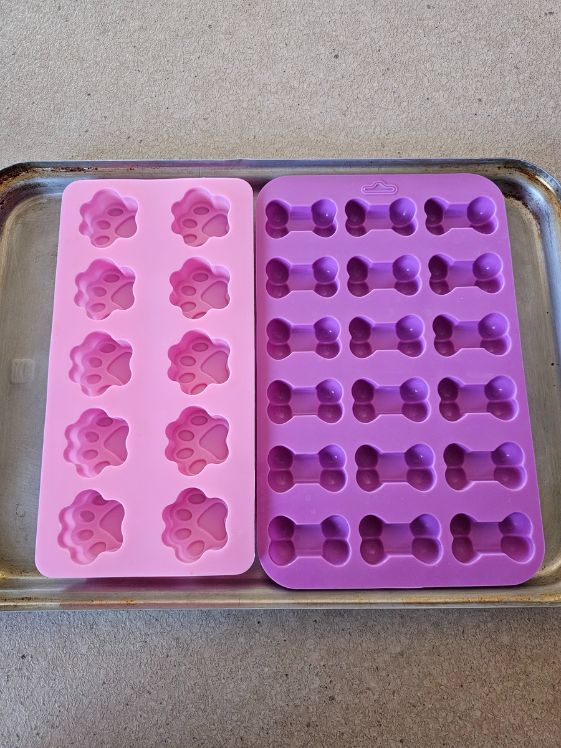 Empty paw and bone shaped silicone molds on a cookie sheeet.