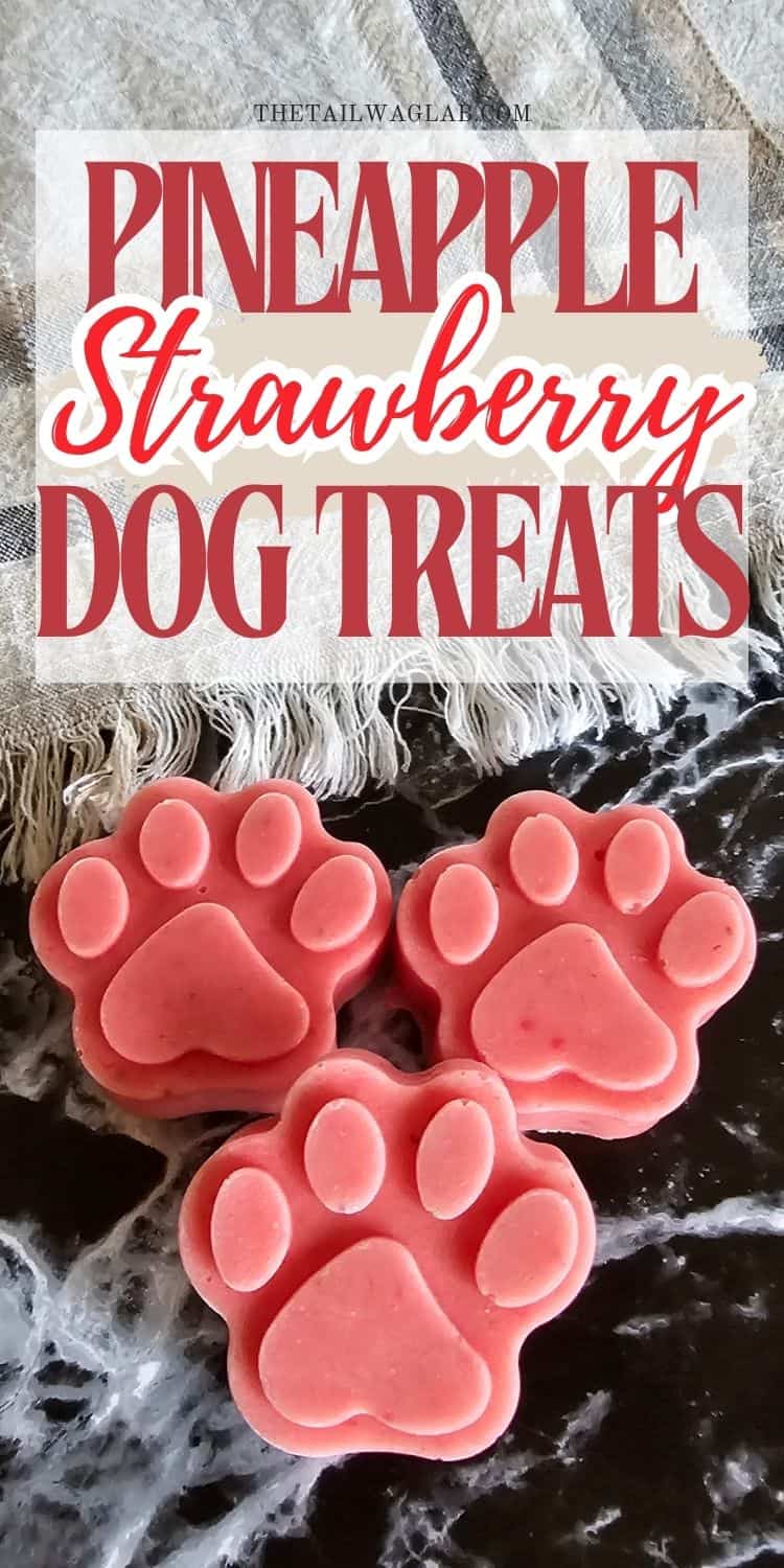 Three paw-shaped frozen dog treats in pink, featuring a mix of pineapple and strawberry flavors, are displayed on a dark surface with a textured background.