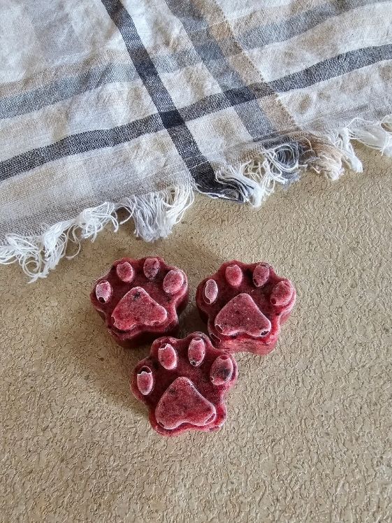 3 paw shaped banana berry dog treats next to a linen towel.