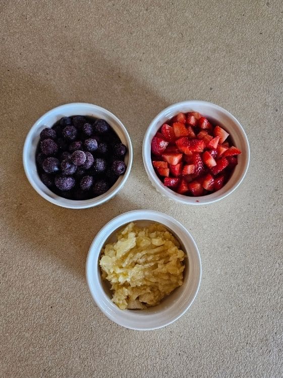 Blueberries, chopped strawberries, and mashed banana in individual white bowls.