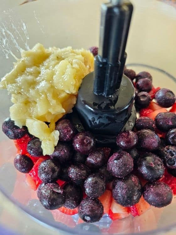 Mashed banana, chopped strawberries, and blueberries in a food processor.
