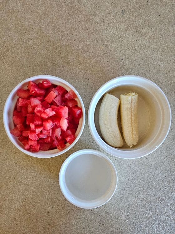Watermelon, banana, and water in white bowls on the counter.