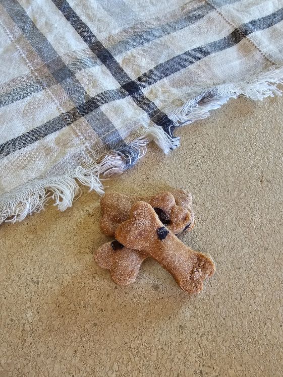 Two bone shaped apple blueberry dog treats next to a linen towel.