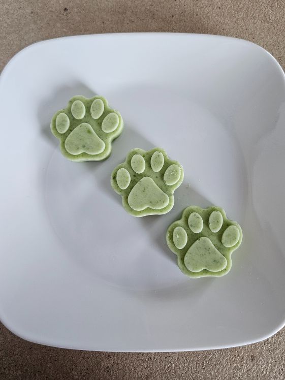 3 paw shaped frozen cucumber yogurt dog treats on a white plate.