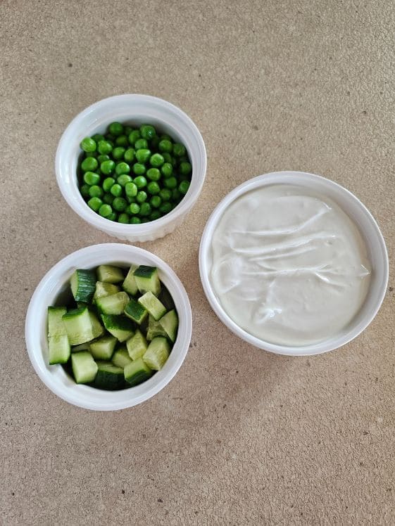 A bowl of peas, a bowl of chopped cucumbers, and a bowl of plain Greek yogurt.