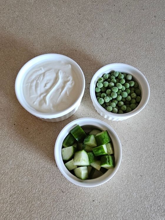 A bowl of peas, a bowl of chopped cucumbers, and a bowl of plain Greek yogurt.