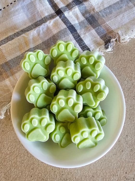 A bowl of paw shaped frozen cucumber yogurt dog treats next to a linen towel.