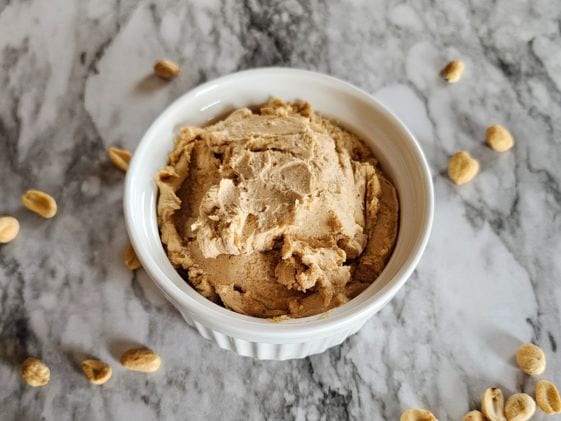 Peanut butter frosting in a white bowl surrounded by peanuts.