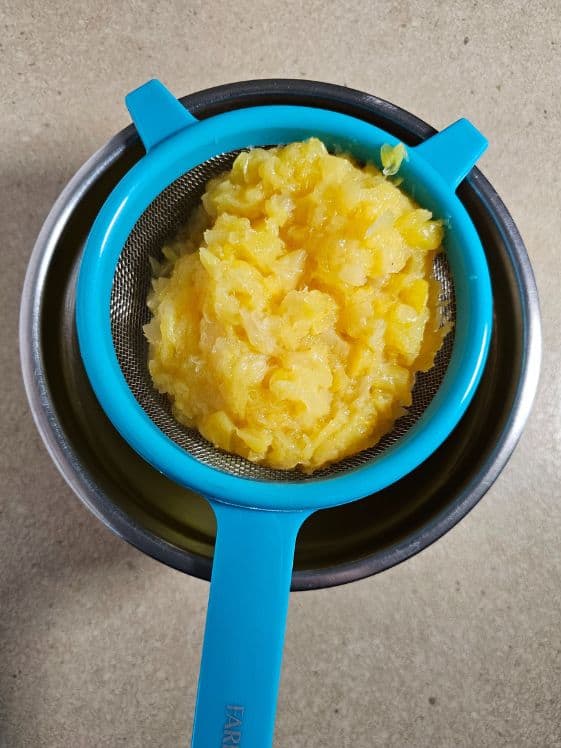 Crushed pineapple in a strainer.