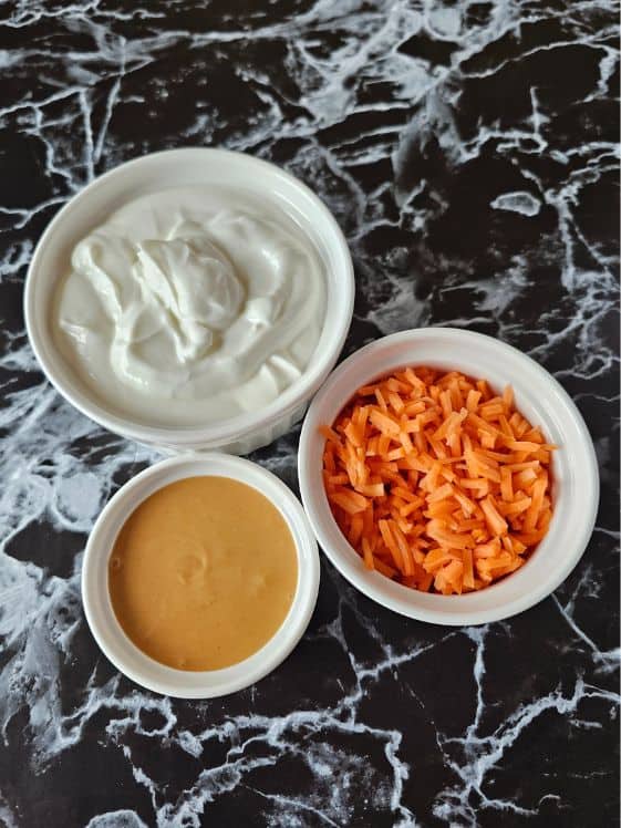 Greek yogurt, shredded carrots, and peanut butter in individual white bowls.