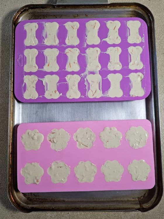 Bone and paw shaped silicone molds filled with carrot, peanut butter, and yogurt mixture.