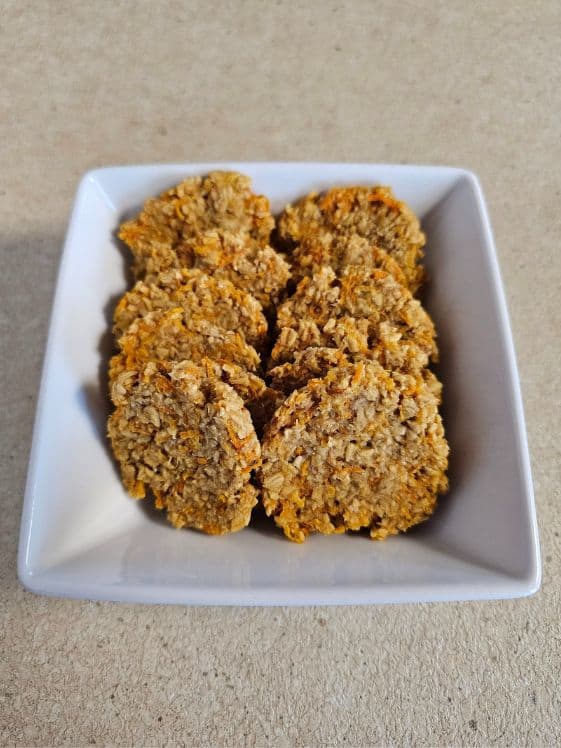 Baked carrot applesauce dog treats in a square white bowl on a counter.