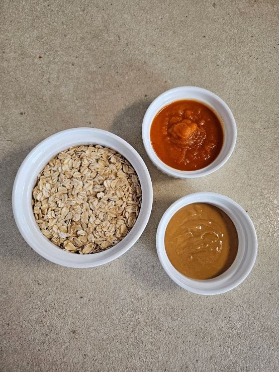 Old fashioned oats, carrot puree, and peanut butter in separate white bowls.