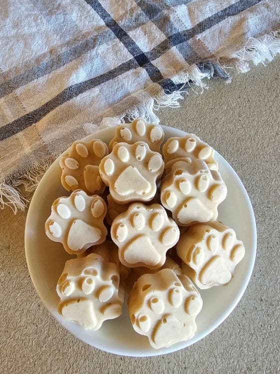 A bowl of paw shaped ice cream for dogs next to a linen towel.