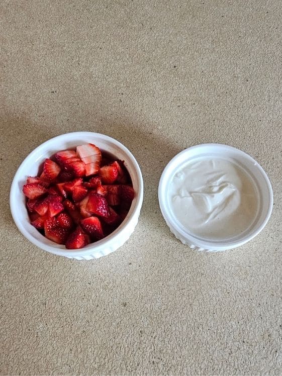 A bowl of chopped strawberries and a second bowl of yogurt.