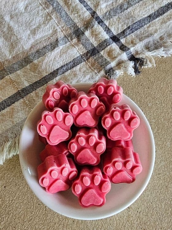 A bowl of paw shaped strawberry ice cream for dogs next to a linen towel.