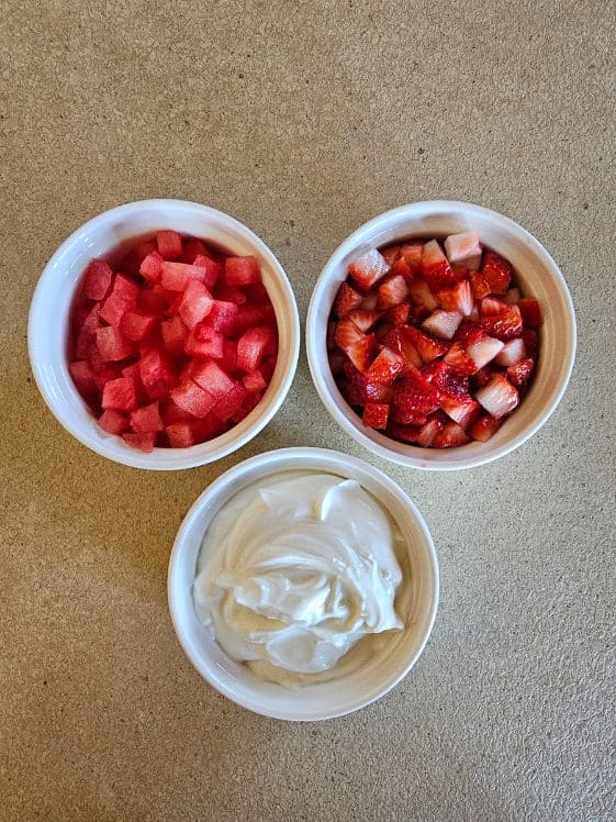 Watermelon, strawberries, and Greek yogurt in white bowls on the counter.