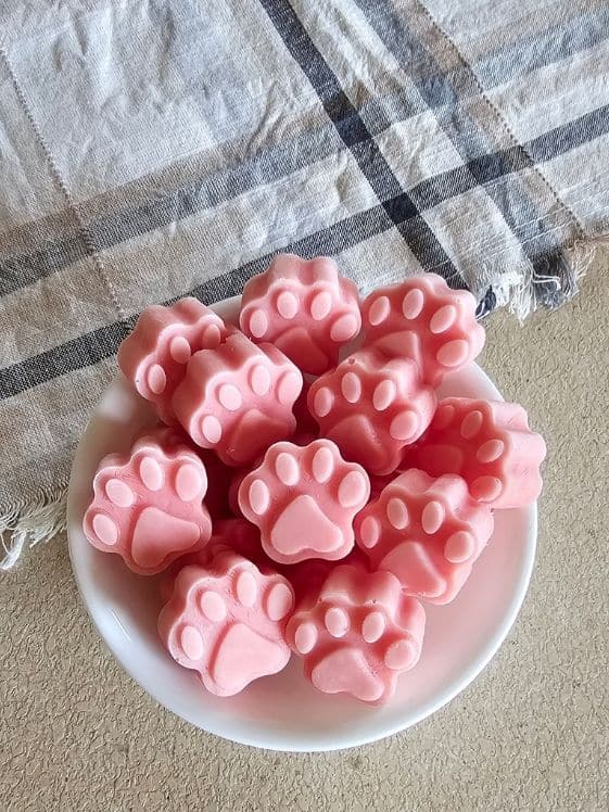 Paw shaped watermelon ice cream for dogs in a white bowl next to a linen towel.