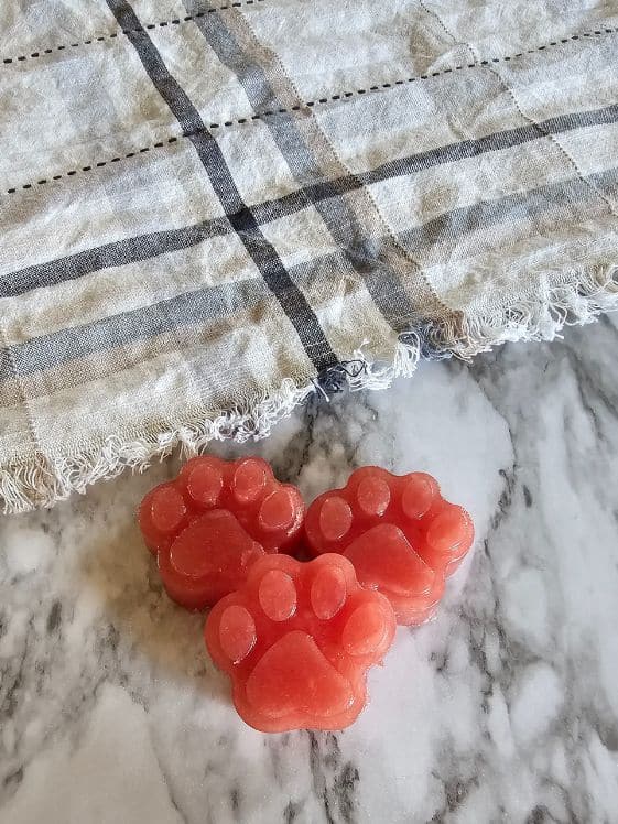 Three paw shaped banana watermelon frozen dog treats next to a kitchen towel.
