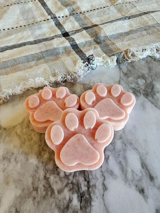 Three paw shaped watermelon ice cream dog treats on a marble surface next to a kitchen towel.