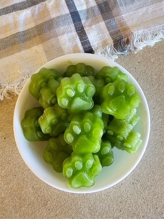 A bowl of paw shaped frozen mint dog treats next to a linen towel.