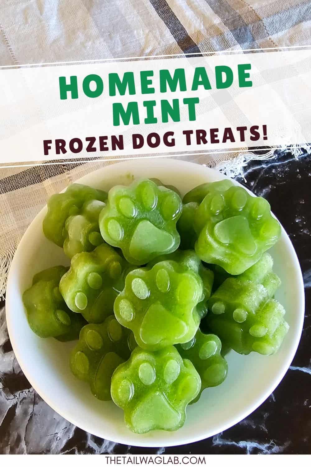 White bowl filled with green paw-shaped frozen dog treats on a neutral surface with a plaid cloth. Text above reads “Homemade Mint Frozen Dog Treats.”