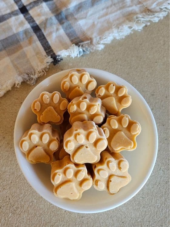 A bowl of paw shaped frozen sweet potato applesauce dog treats next to a linen towel.