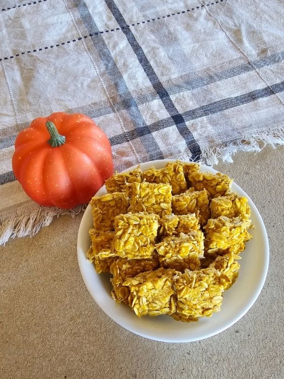 A bowl of no bake apple pumpkin bites next to a small pumpkin and linen towel.