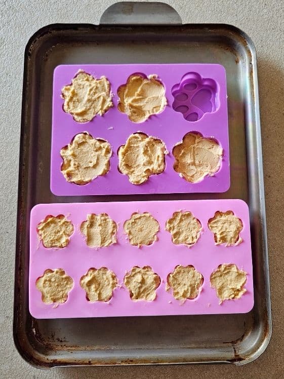Paw shaped silicone molds filled with peanut butter sweet potato dog treat mixture.