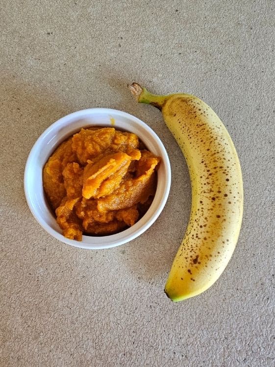 A white bowl with pumpkin puree next to a ripened banana.